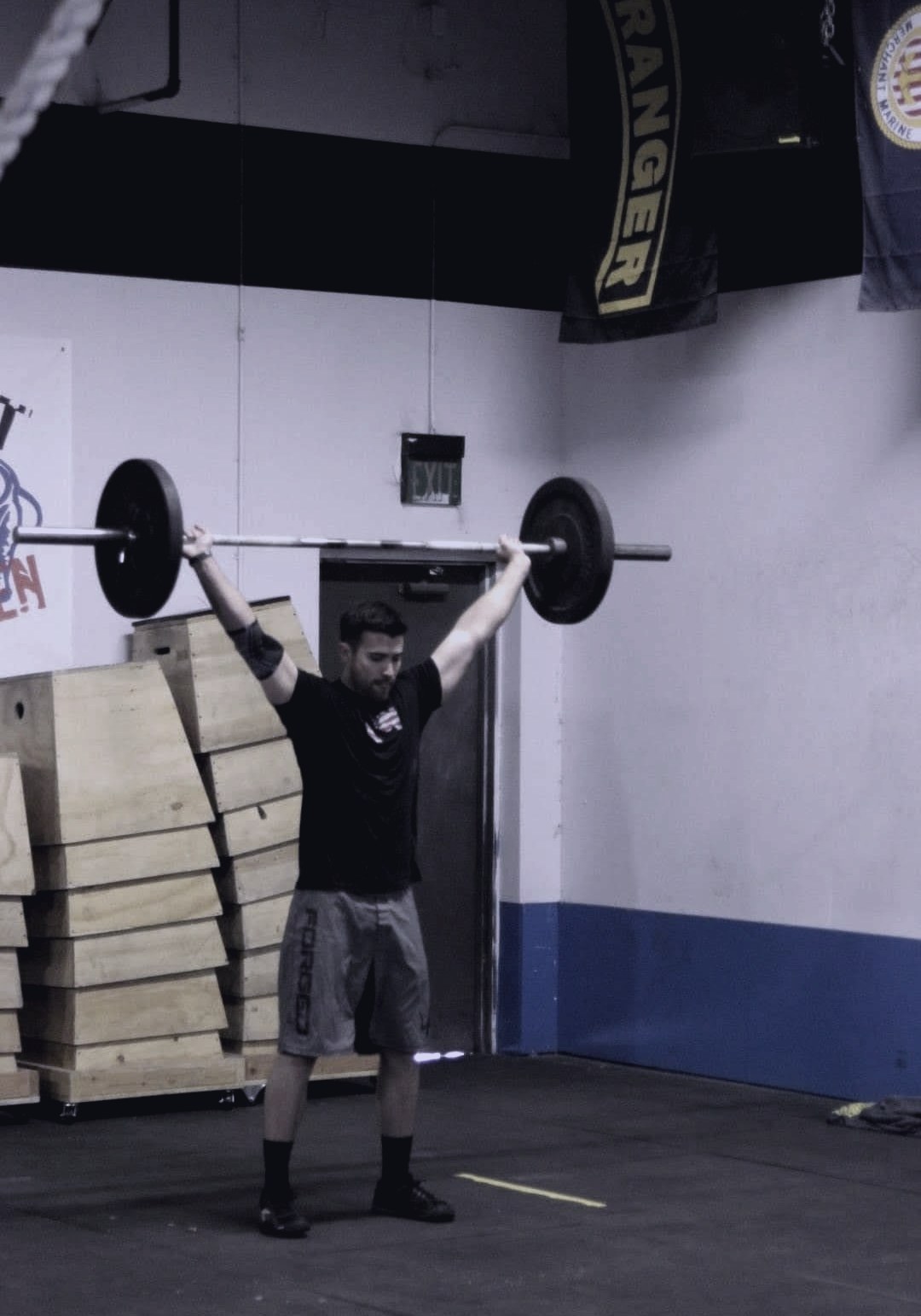 RK locking out a barbell overhead in a CrossFit gym.