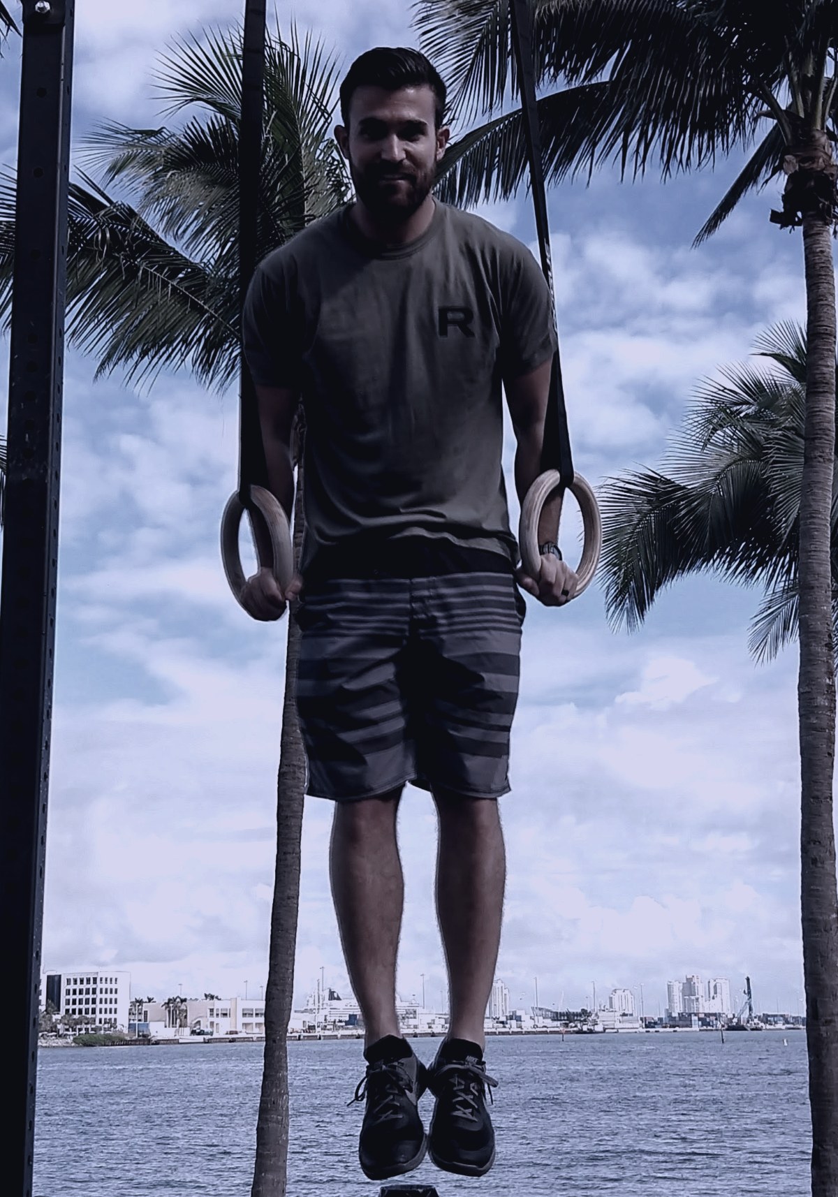 RK hanging from gymnastic rings outdoors in Miami.